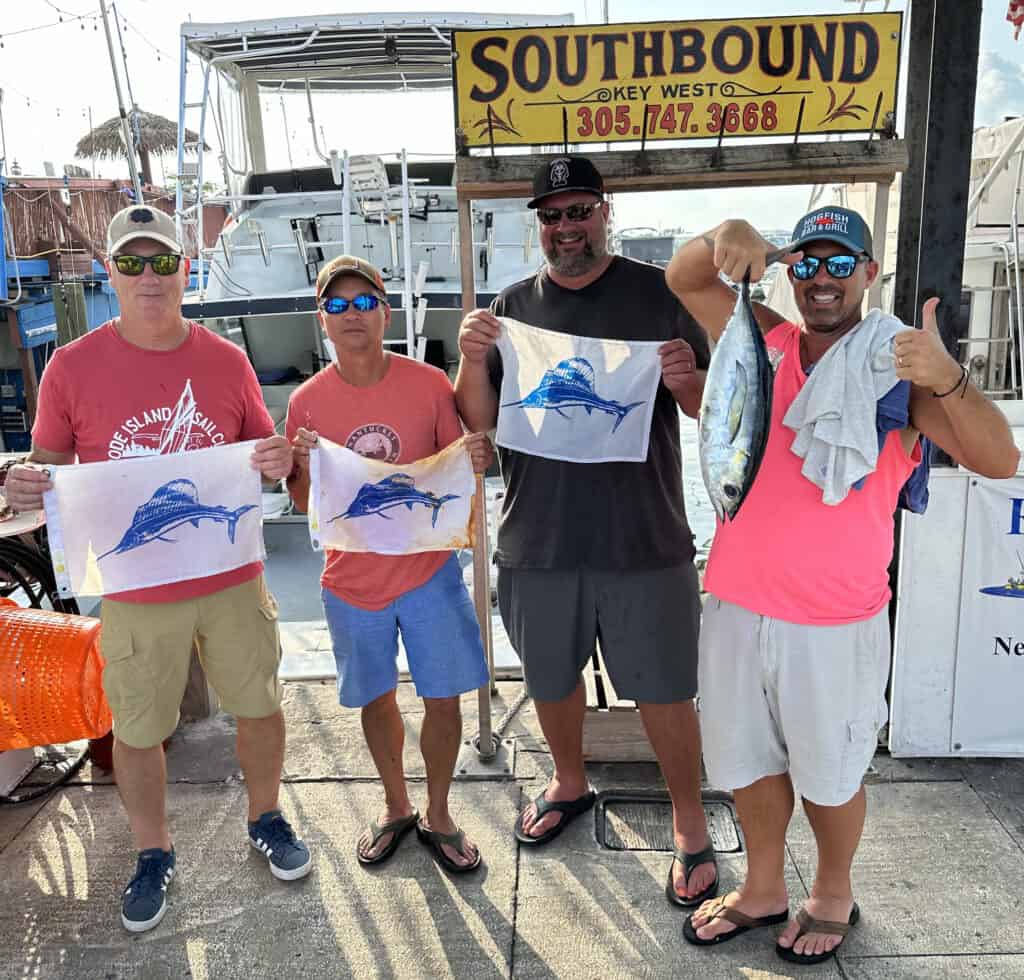4 men holding 3 sailfish flags and a tuna on the dock